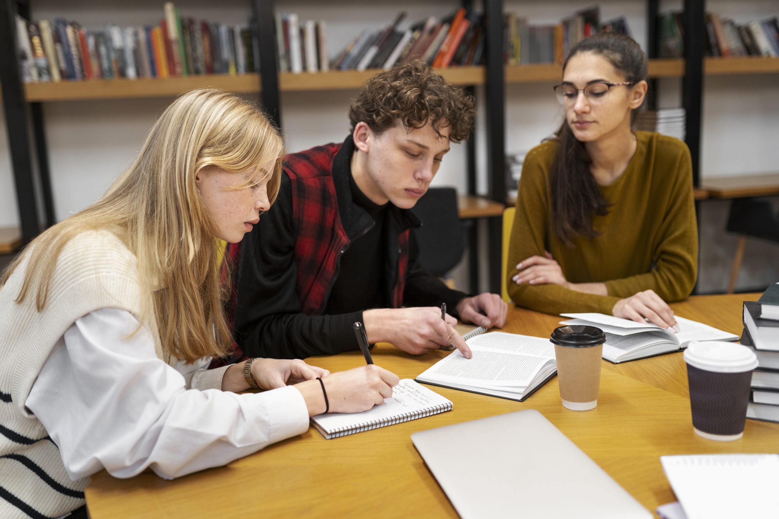 A graduate student looking focused while studying a large stack of academic books and notes.